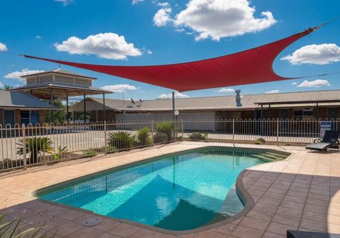 Outdoor swimming pool with red shade sail, brick building, and manicured garden