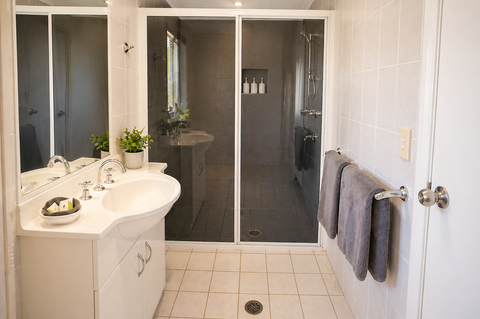 Spacious ensuite with dual curved vanity, large mirror, dual walk-in showers, grey tiles