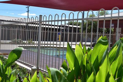 Swimming pool behind white fencing with red shade sail and landscaping